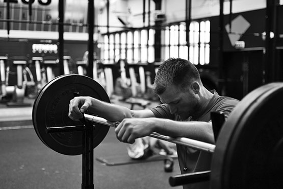 Man leaning on his barbell set in the gym whilst training his breathe before lifting weights.