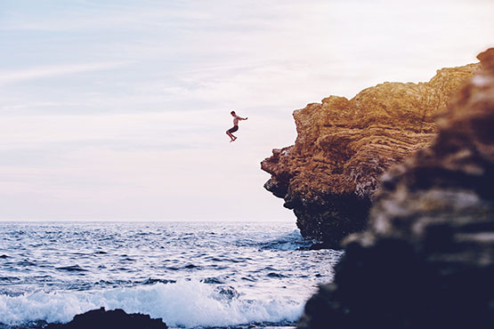 Man jumping from the cliff to the open water in his swimming shorts.